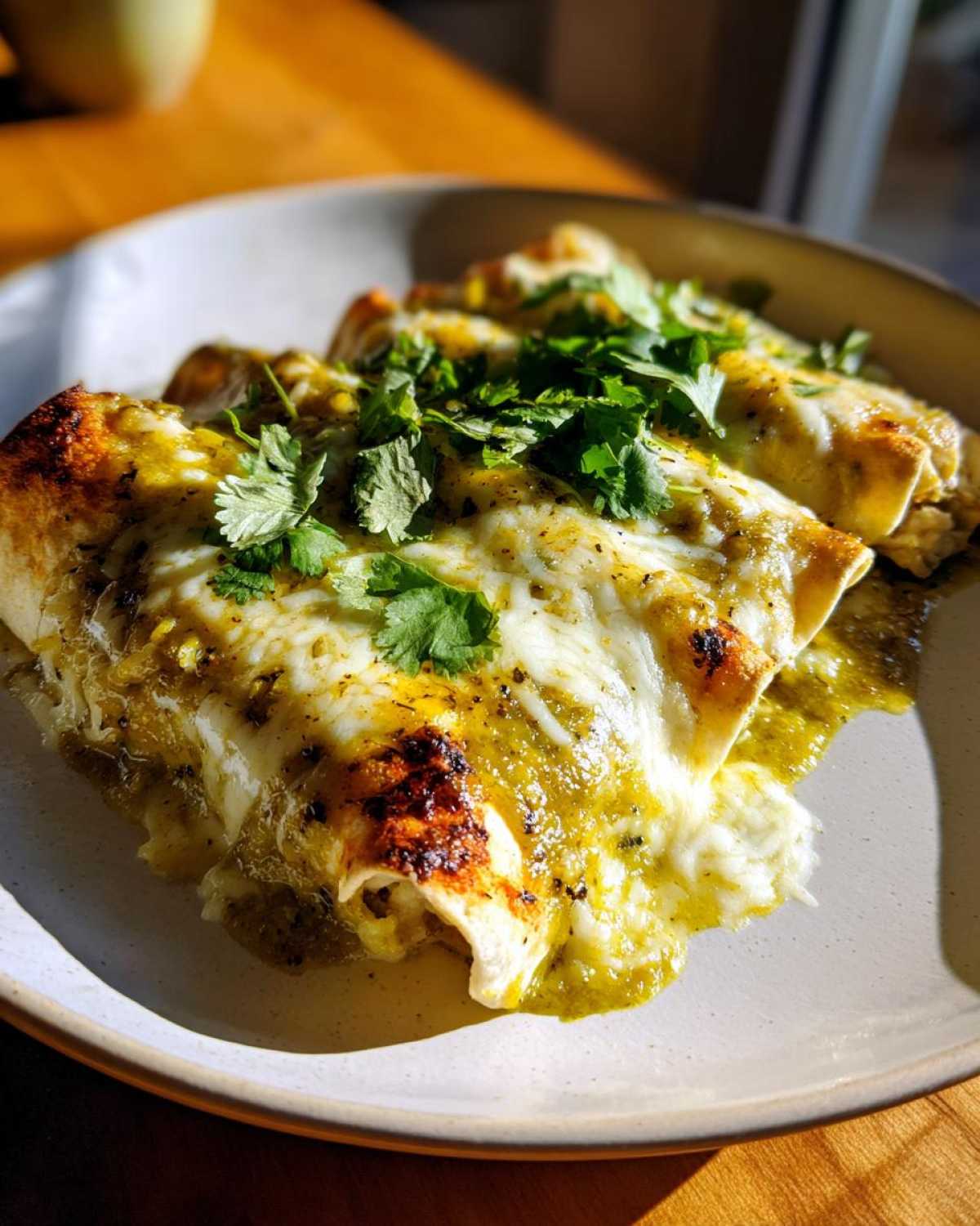 Close-up of cheesy green chile chicken enchiladas topped with fresh cilantro.
