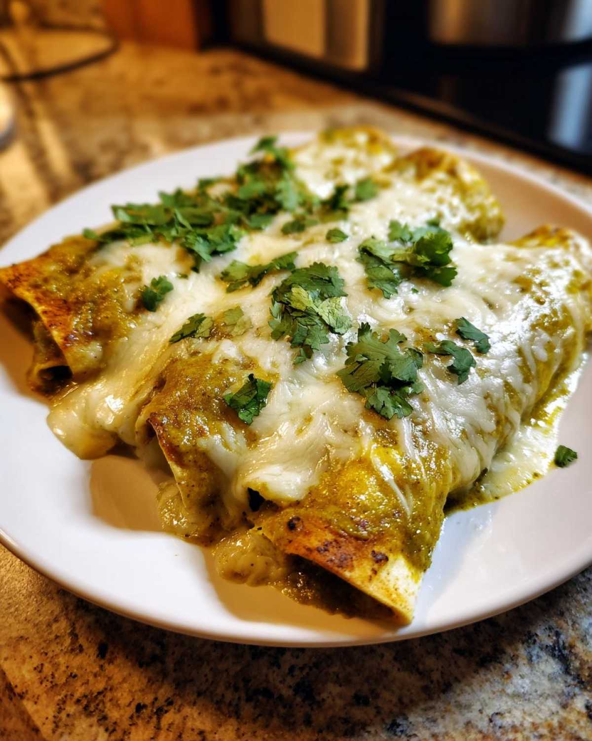 Close-up of three green chile chicken enchiladas smothered in melted white cheese and fresh cilantro.
