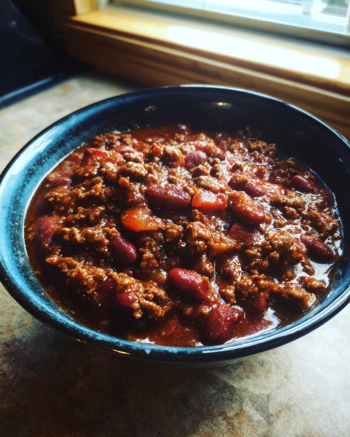 Close-up of a dark blue bowl filled with rich, hearty chili featuring ground meat and kidney beans.
