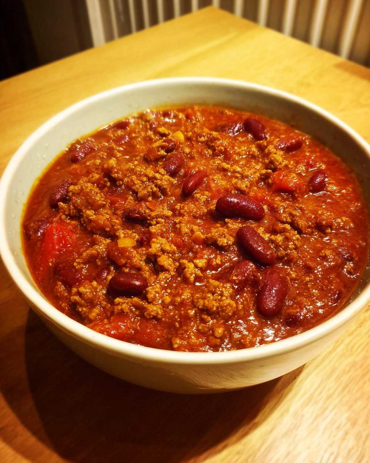 Close-up of a white bowl filled with rich, thick crockpot chili featuring ground meat and dark red kidney beans.