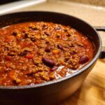 Close-up of rich, thick crockpot chili filled with ground meat and kidney beans in a dark cooking pot.