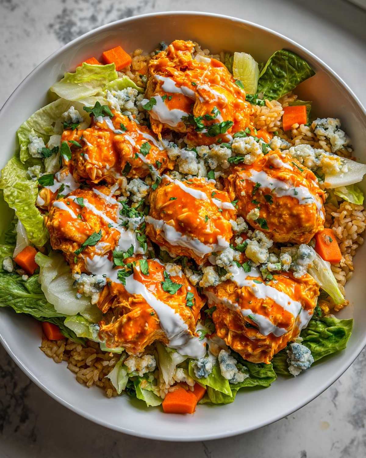 Overhead view of a vibrant buffalo chicken bowl featuring orange-sauced chicken, blue cheese, lettuce, and brown rice.