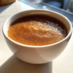 Close-up of homemade applesauce, rich brown in color, sprinkled with cinnamon, served in a white bowl.
