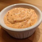Close-up of creamy, orange-hued big mac sauce speckled with spices in a small white dipping bowl.