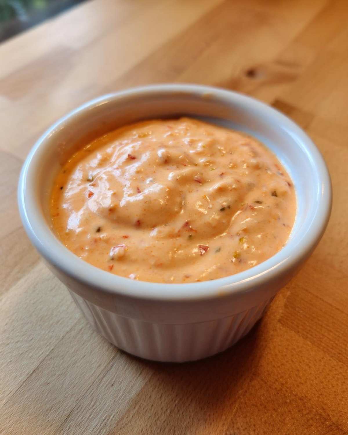 Close-up of creamy, orange-pink big mac sauce speckled with relish in a small white dipping bowl.