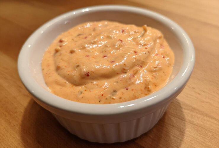 Close-up of creamy, orange-hued big mac sauce speckled with spices in a small white dipping bowl.