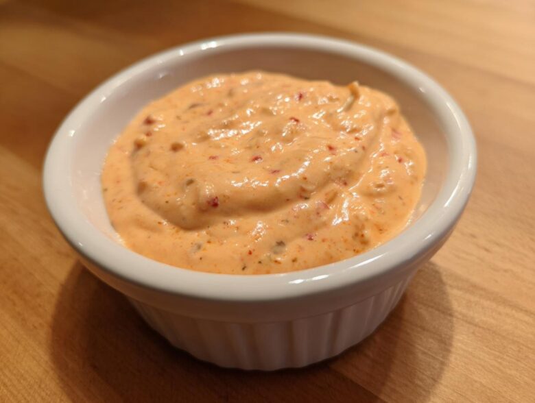 Close-up of creamy, orange-hued big mac sauce speckled with spices in a small white dipping bowl.