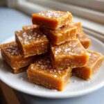 A stack of chewy, square pieces of homemade caramel topped with flaky sea salt.