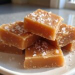 A stack of freshly cut, rich brown squares of homemade caramel topped with flaky sea salt.