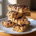 A stack of five homemade protein bars drizzled with dark chocolate, resting on a white plate.