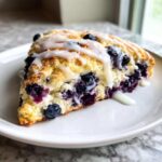 A close-up of a triangular slice of homemade blueberry scones topped with a sweet white glaze.