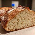 Close-up of a freshly baked Italian bread loaf cut in half, showing the open, airy crumb structure and golden crust.