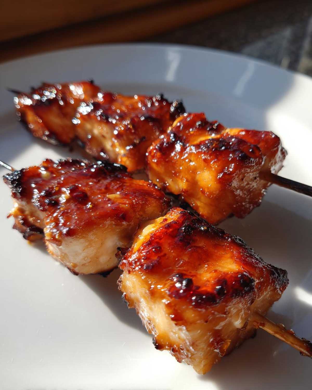 Close-up of two perfectly grilled, glazed chicken skewers with caramelized edges resting on a white plate.