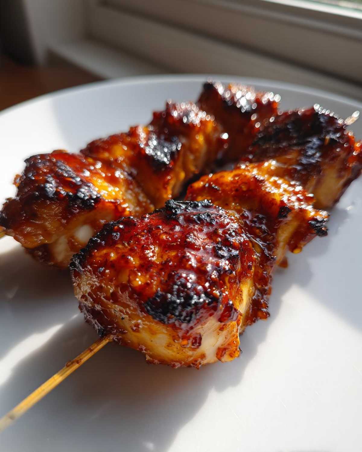 Close-up of two juicy, glazed, and slightly charred chicken skewers resting on a white plate.