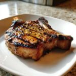 Close-up of a perfectly grilled, thick-cut bone-in pork chop showing char marks, suggesting a great marinade for pork chops.