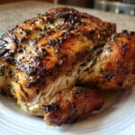 A perfectly roasted, herb-crusted spatchcock chicken resting on a white plate, showing golden-brown, crispy skin.