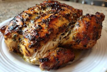 A perfectly roasted, herb-crusted spatchcock chicken resting on a white plate, showing golden-brown, crispy skin.
