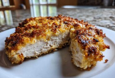 Close-up of juicy parmesan crusted chicken cut in half, showing the white interior and golden brown crust.
