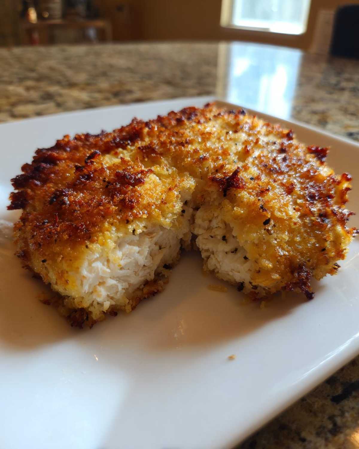 Close-up of juicy parmesan crusted chicken cut open to show the white, cooked interior.