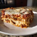 A thick, layered slice of Lasagna with Cottage Cheese, topped with melted mozzarella and herbs.