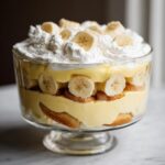 Close-up of a layered banana pudding trifle featuring vanilla wafers, creamy pudding, fresh banana slices, and whipped cream topping.