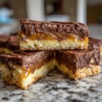 Close-up of stacked twix cookies bars showing shortbread base, caramel layer, and chocolate topping.