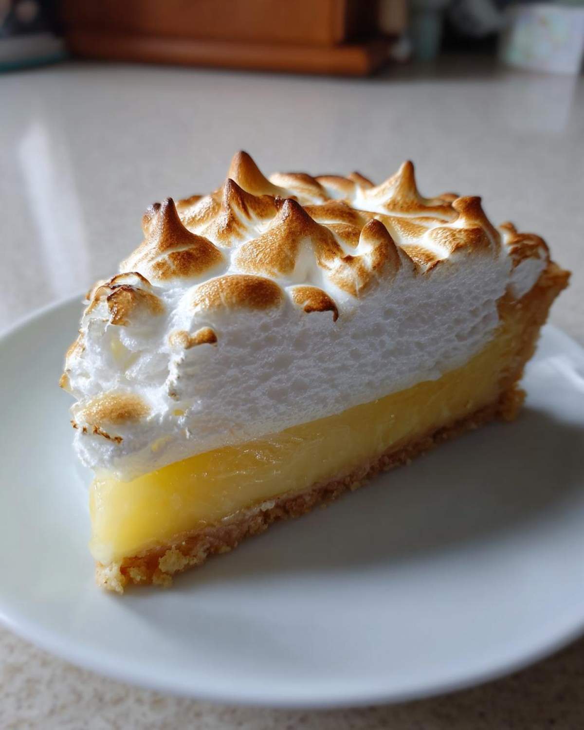 A close-up slice of lemon meringue pie showing tall, perfectly torched peaks on the meringue topping.
