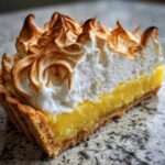 Close-up of a slice of lemon meringue showing tall, perfectly torched meringue peaks over bright yellow lemon filling.