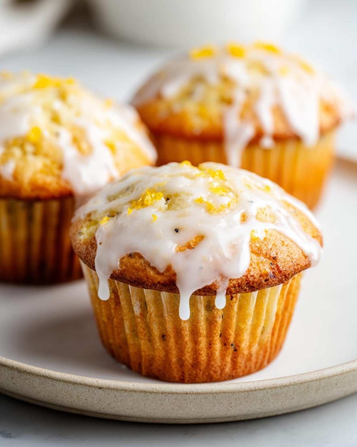 Close-up of three moist lemon poppy seed muffins topped with white glaze and bright yellow zest.