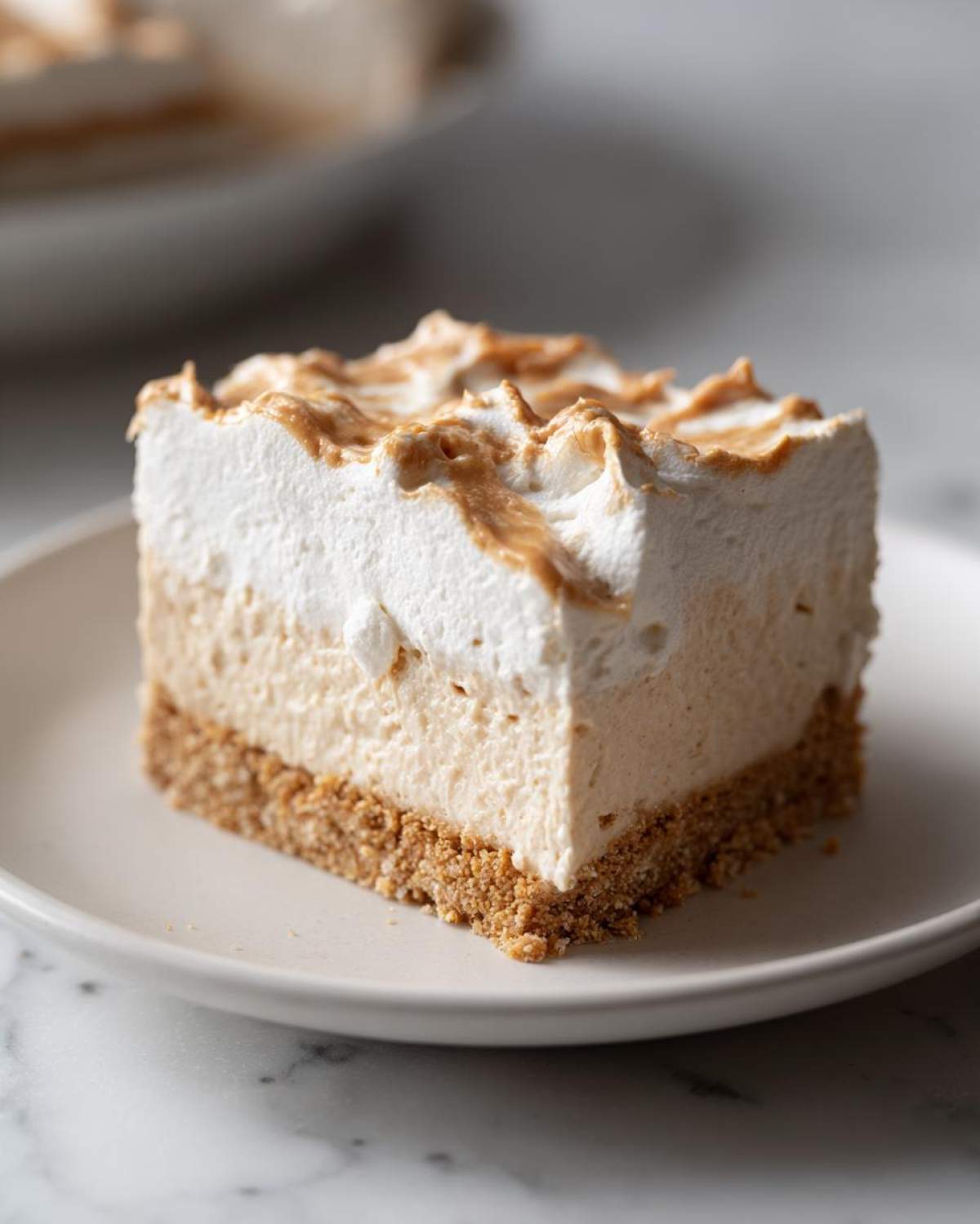 Close-up of a square slice of low-calorie peanut butter pie with a graham cracker crust and whipped topping.