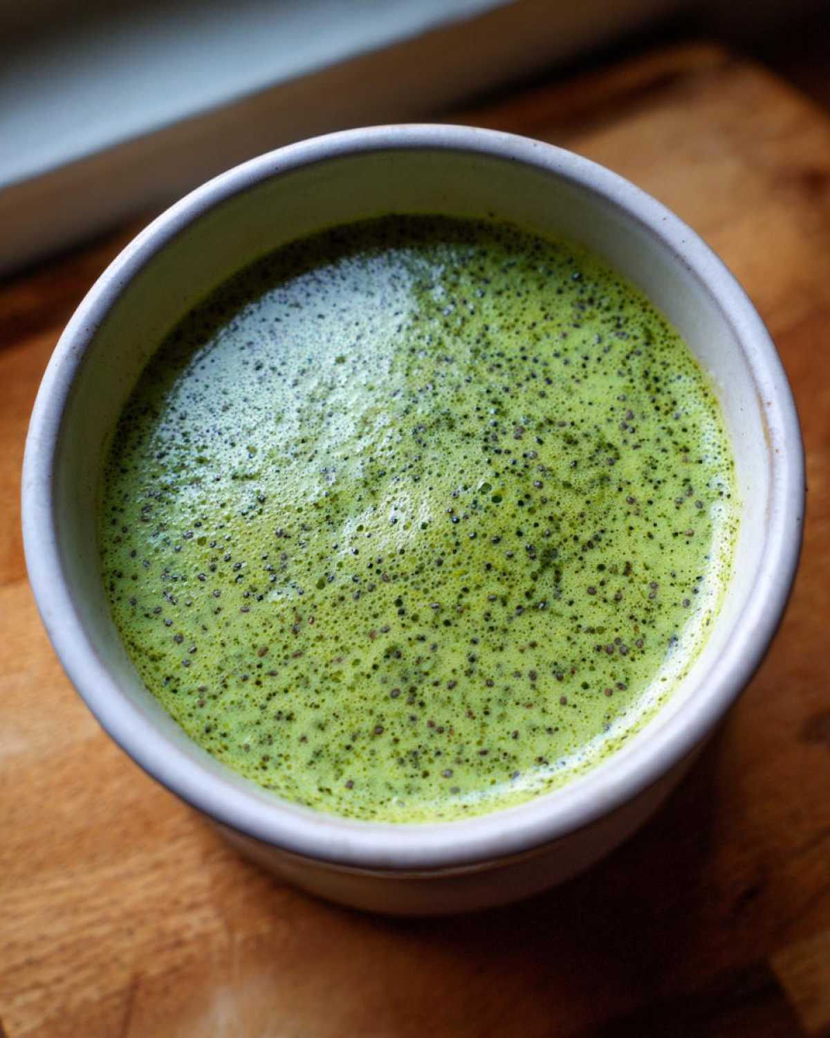 Overhead view of creamy, bright green matcha chia pudding topped with visible chia seeds in a light-colored bowl.
