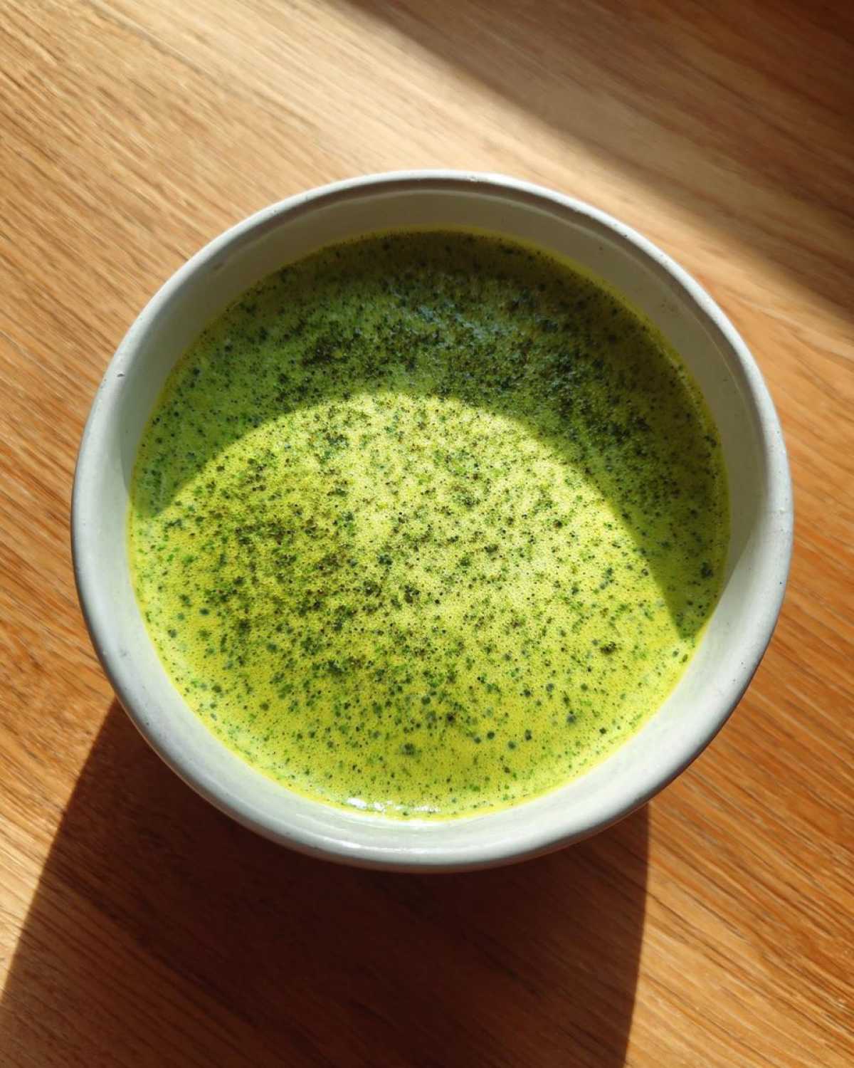 Overhead view of vibrant green matcha chia pudding in a light bowl on a wooden surface.