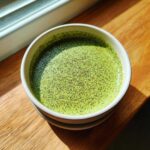 Overhead view of vibrant green matcha chia pudding topped with small dark specks, served in a white bowl.