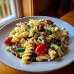 Close-up of a bowl of creamy mediterranean pasta salad featuring rotini, cherry tomatoes, cucumbers, olives, and feta cheese.