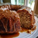 Close-up of a slice cut from a bundt-style apple dapple cake covered in thick caramel sauce.
