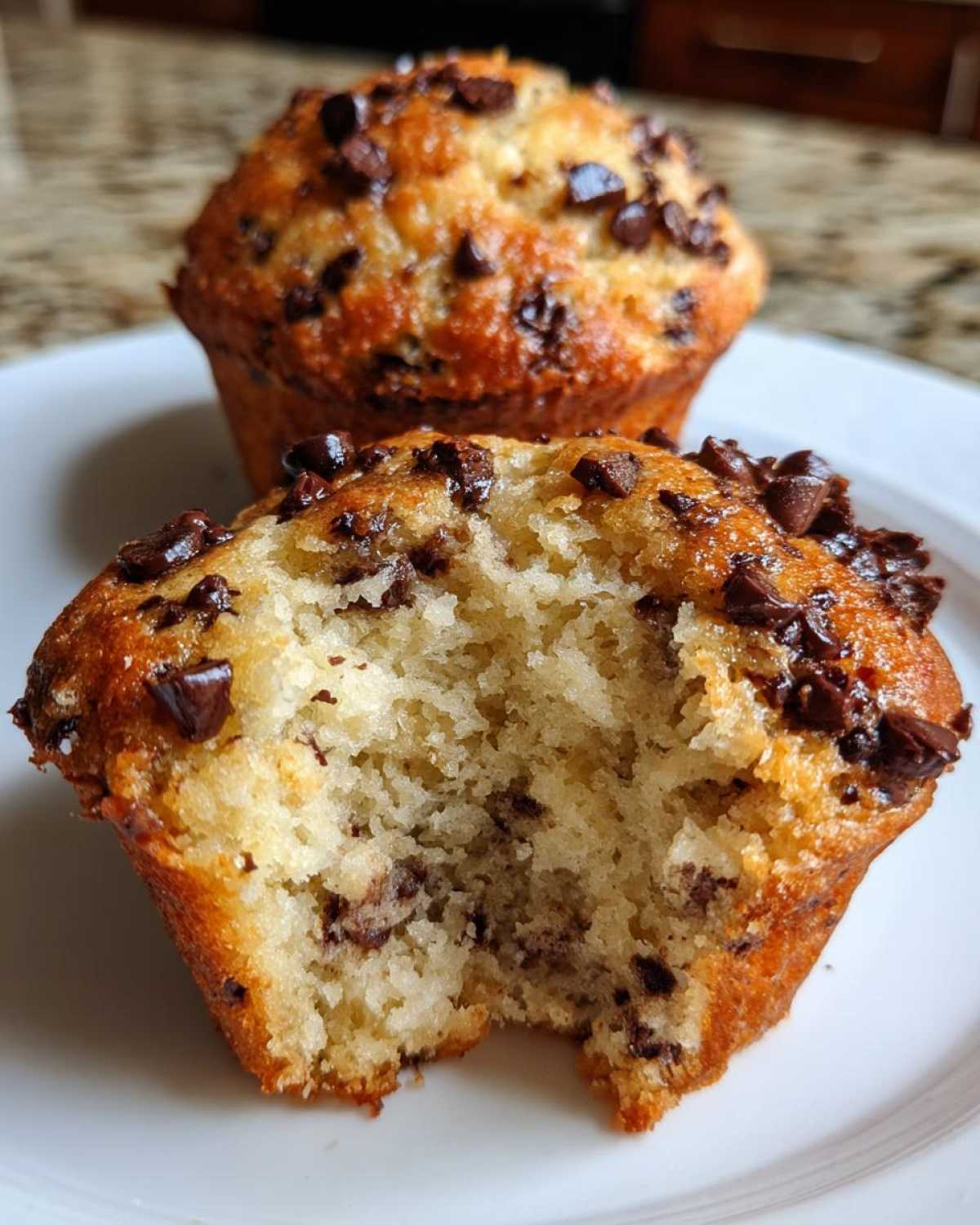 Close-up of a moist banana chocolate chip muffin with a bite taken out, showing the fluffy interior and chocolate chips.
