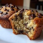 Close-up of a moist banana chocolate chip muffin with a bite taken out, showing the soft interior and chocolate chips.