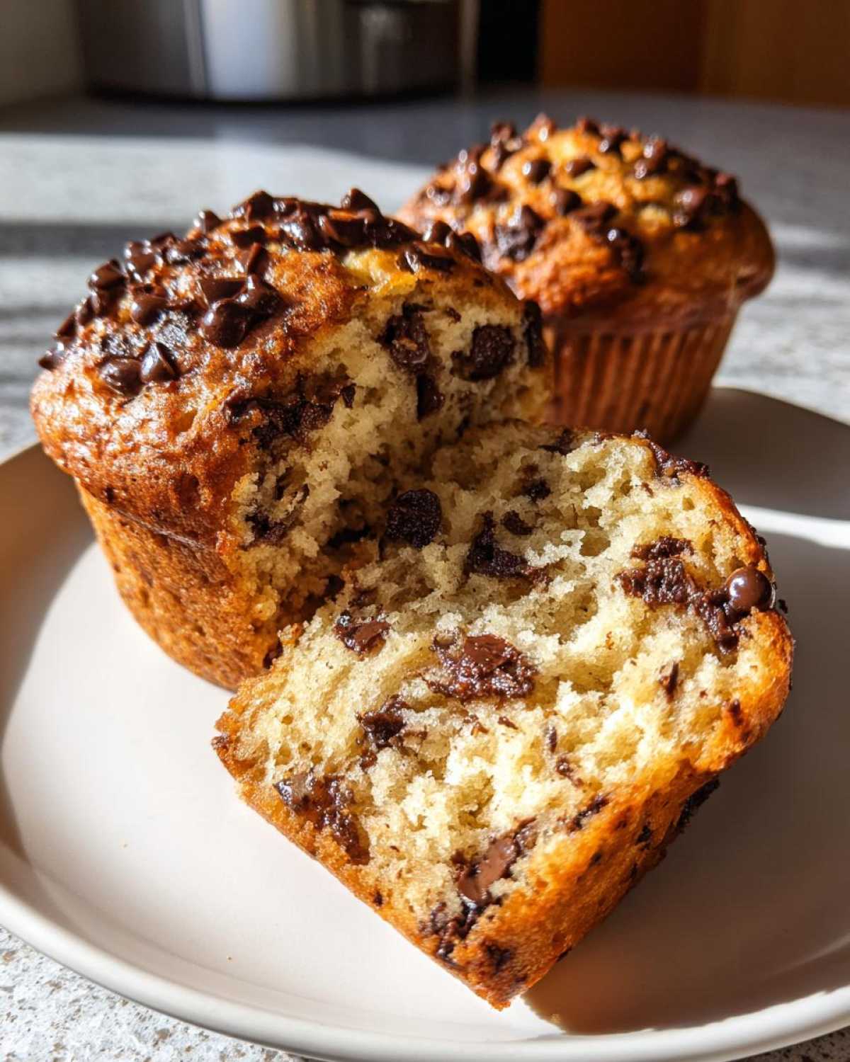 Close-up of a moist banana chocolate chip muffin cut in half, showing the soft interior and melted chocolate chips.