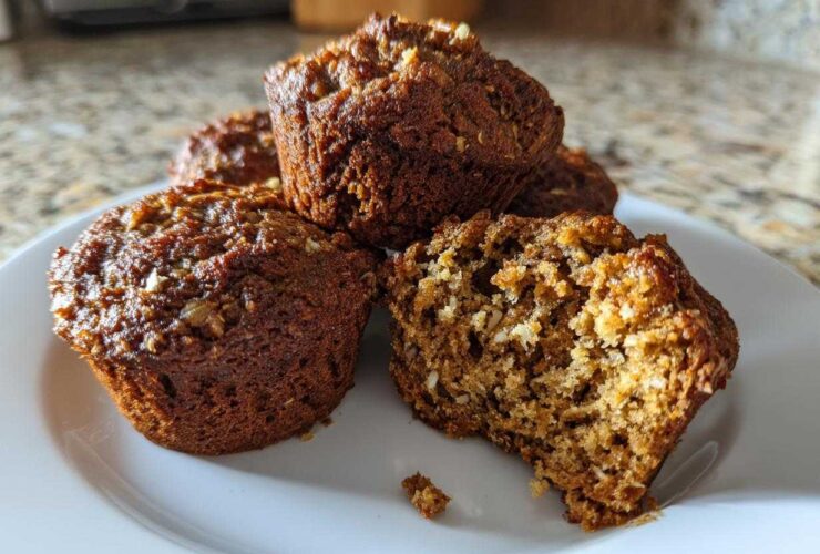 A close-up of several moist bran muffins on a white plate, one cut open showing the texture.