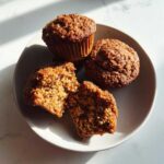 Close-up of moist bran muffins on a plate, one broken open to show the soft, textured interior.