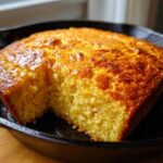 Close-up of moist buttermilk cornbread with a golden-brown crust, served in a black cast iron skillet.