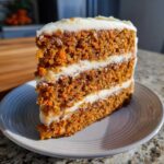Close-up of a thick slice of moist carrot cake recipe with three layers and cream cheese frosting.