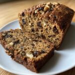 Close-up of moist date nut bread loaf with two slices cut, showing raisins and walnuts throughout.