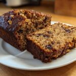 Two slices of moist date nut bread, rich in dark dates and walnuts, served on a white plate.