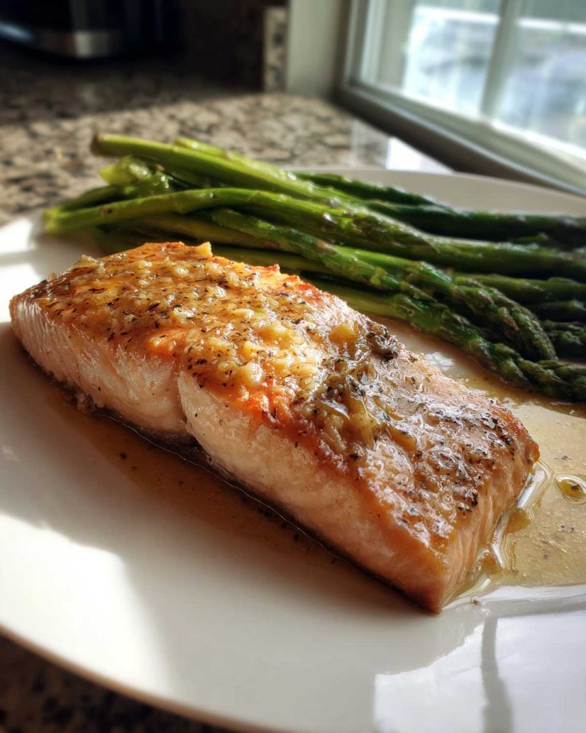 A beautifully cooked salmon recipe fillet, glazed and served next to bright green asparagus spears.