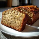 Close-up of a thick slice of moist greek yogurt banana bread with a golden-brown crust on a white plate.