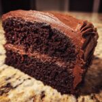 Close-up of a rich, dark slice of homemade chocolate cake covered in thick chocolate frosting.