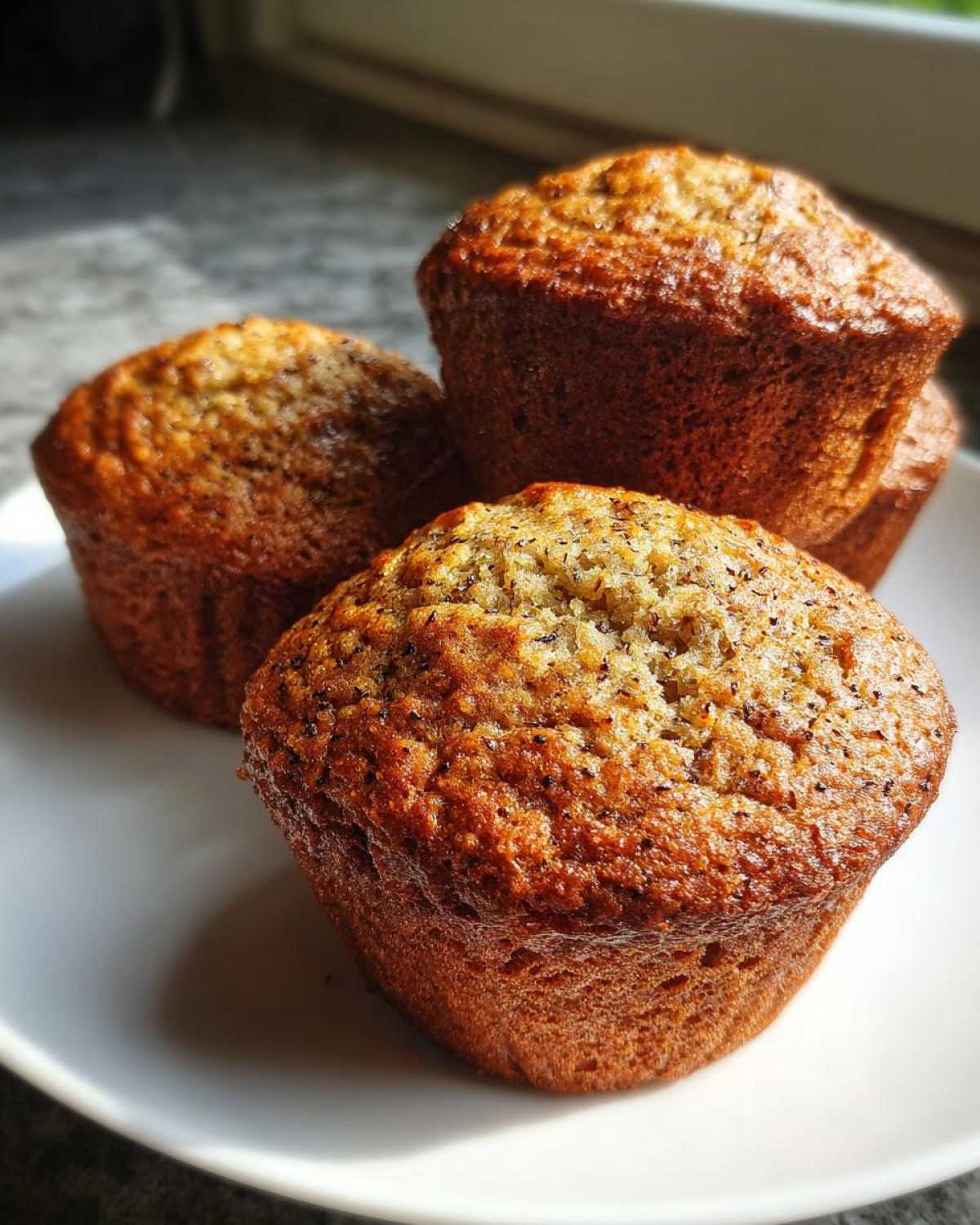 Close-up of three golden brown honey bran muffins stacked slightly on a white plate.