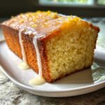 A close-up of a moist slice of lemon pound cake drizzled with white glaze and topped with zest.