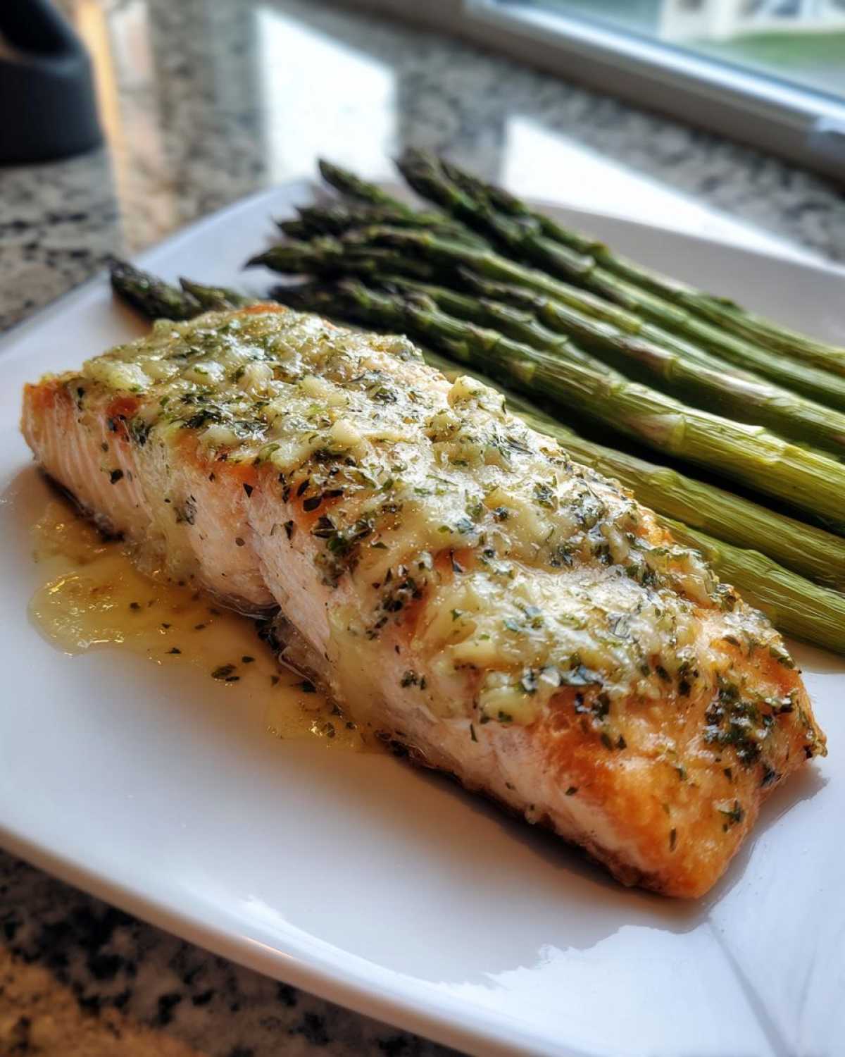 A perfectly cooked salmon recipe fillet topped with melted garlic herb butter, served next to roasted asparagus.